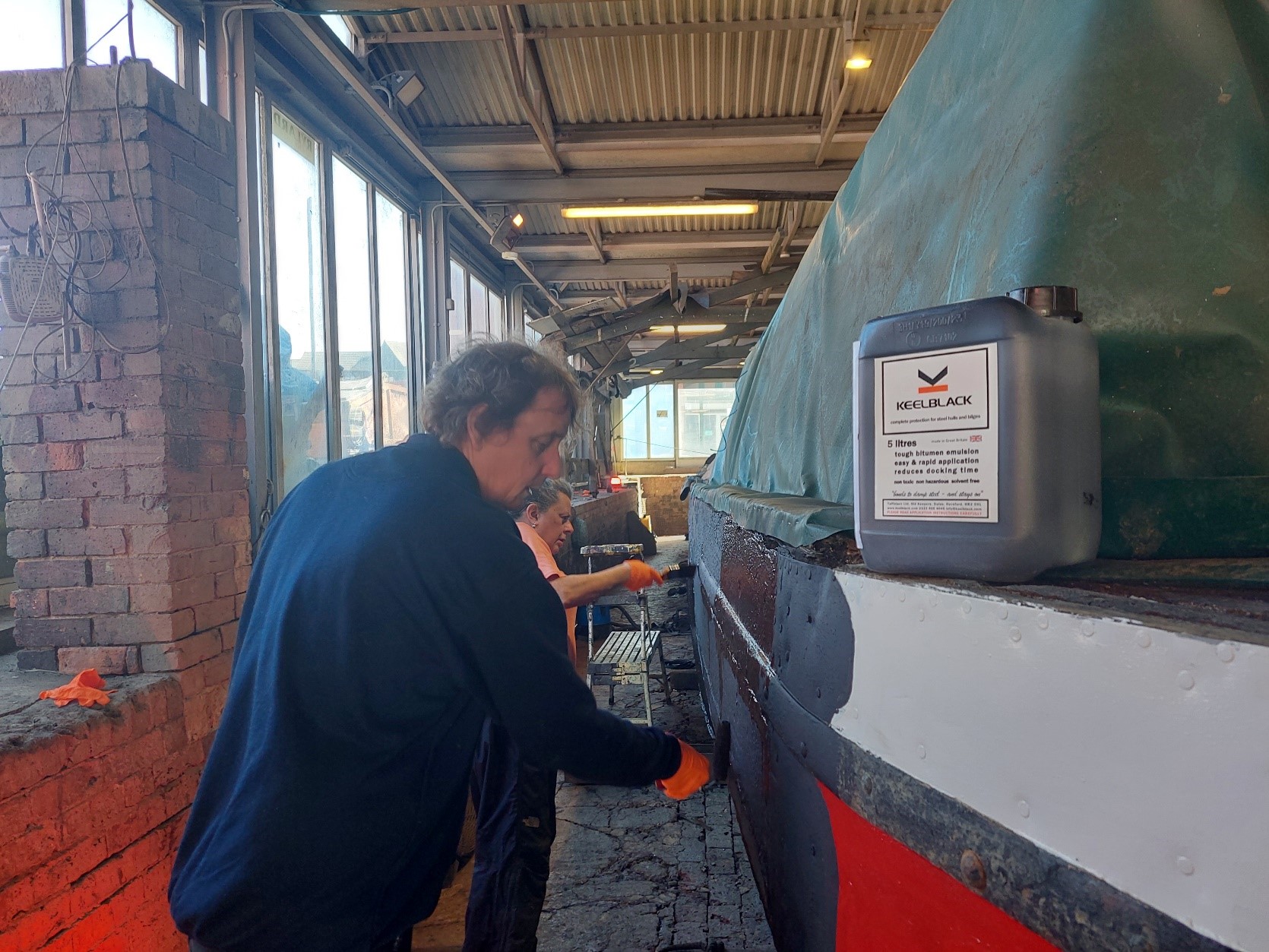 Two people working on blacking the hull of Hardy