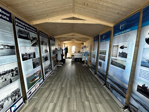 View inside the exhibition space, with wooden floor panelling and tall posters on both sides