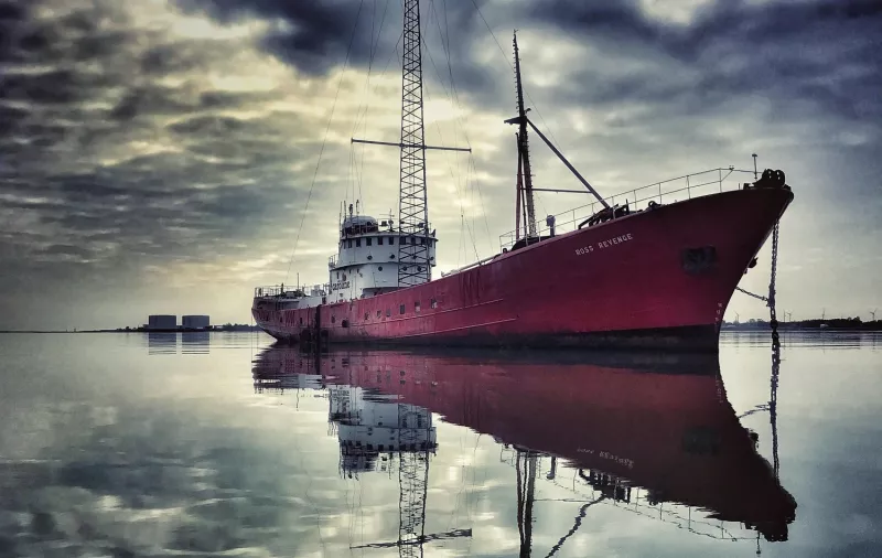 Starboard bow view of MV Ross Revenge on a backdrop of dramatic cloudy sky reflected in the water below